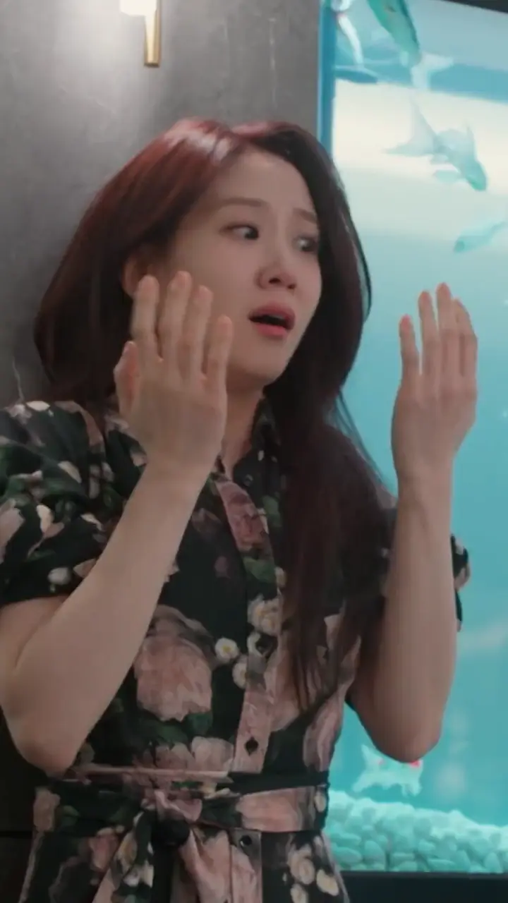 Yeo-ri, in a floral dress, throws up both hands in front of an aquarium